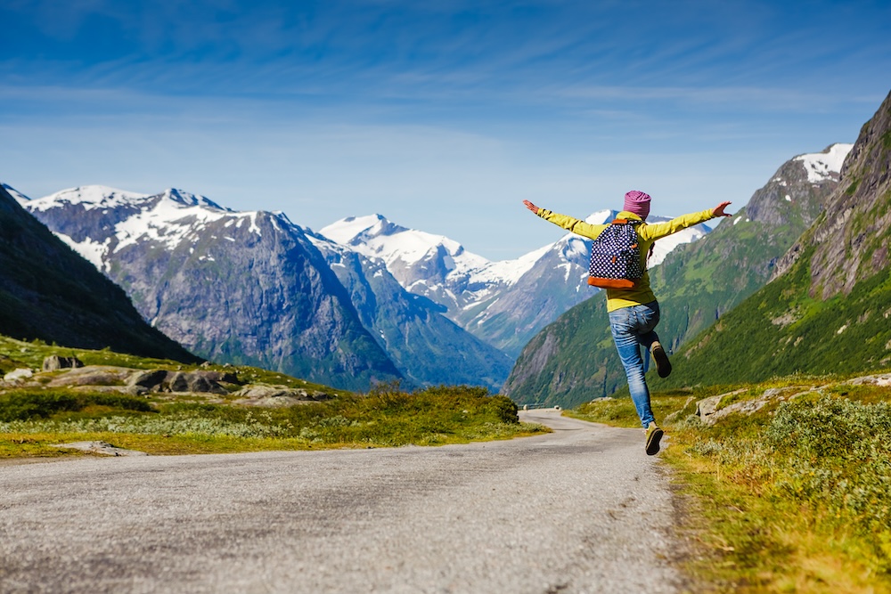 Hiker jumping on road with snowy mountains