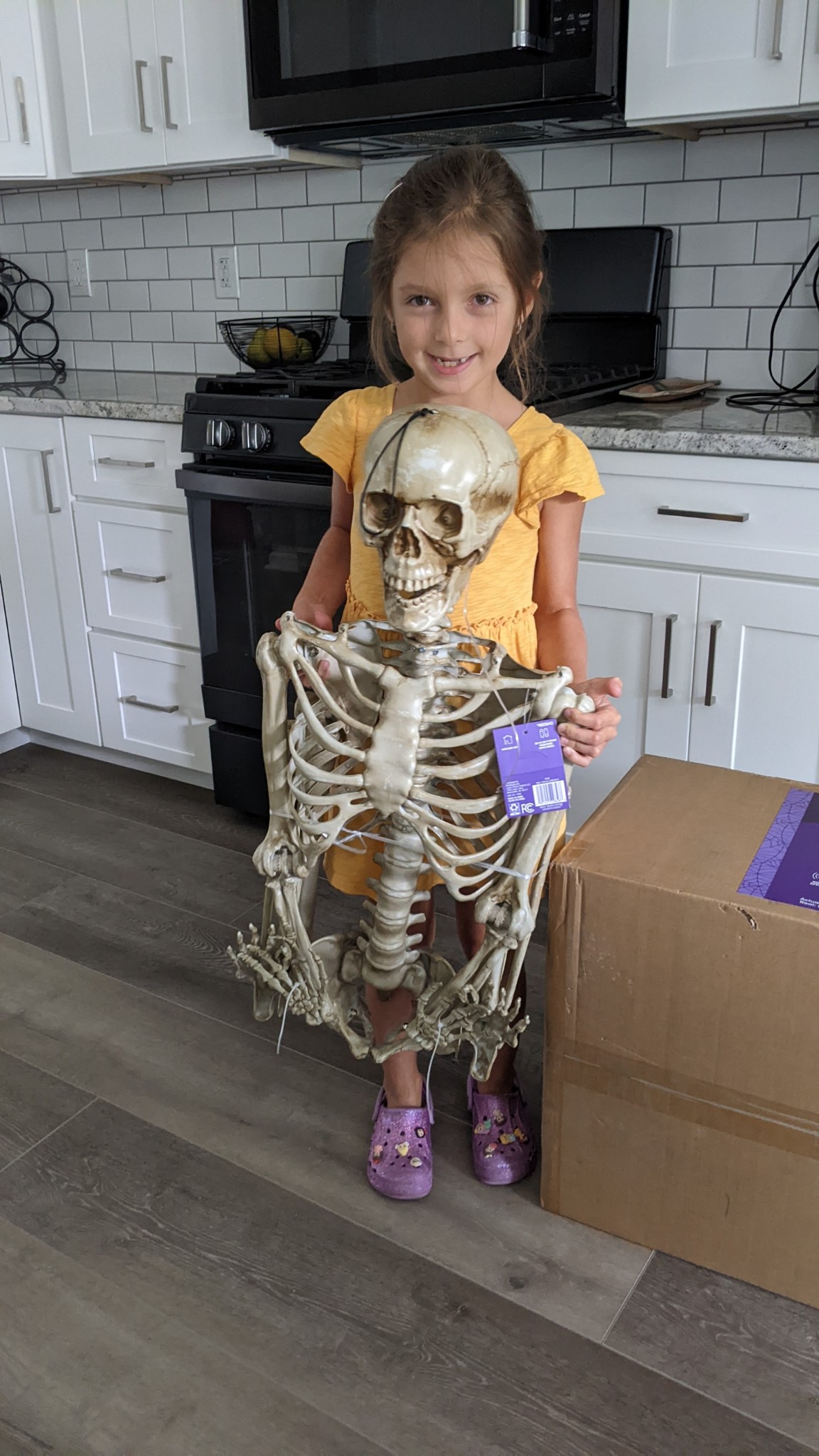 Smiling girl holding plastic skeleton in kitchen