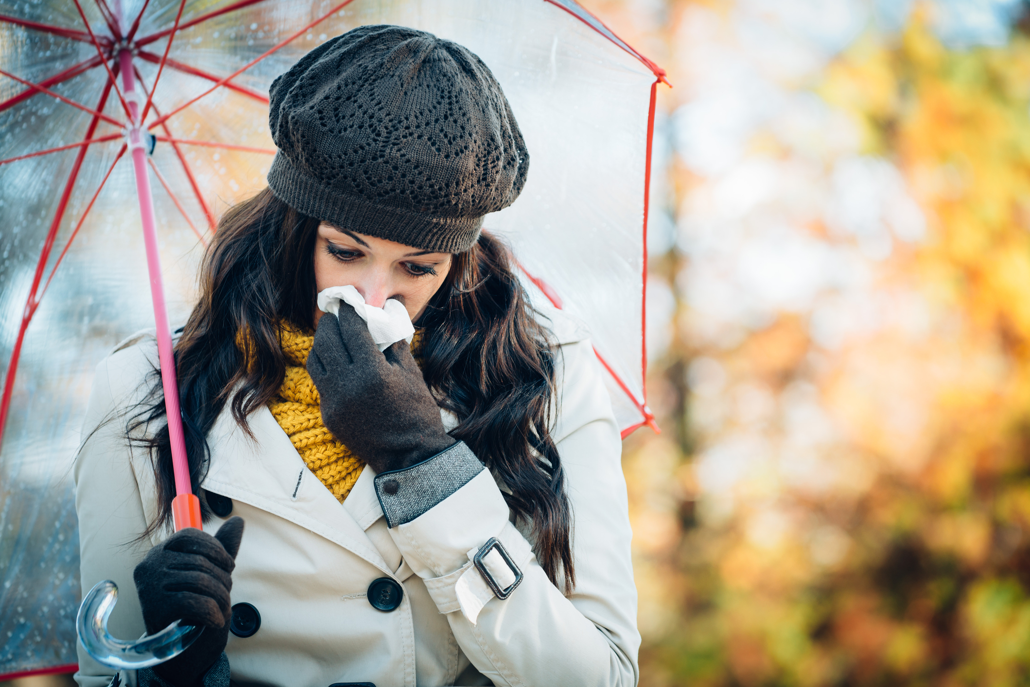 Woman blowing nose under umbrella in autumn